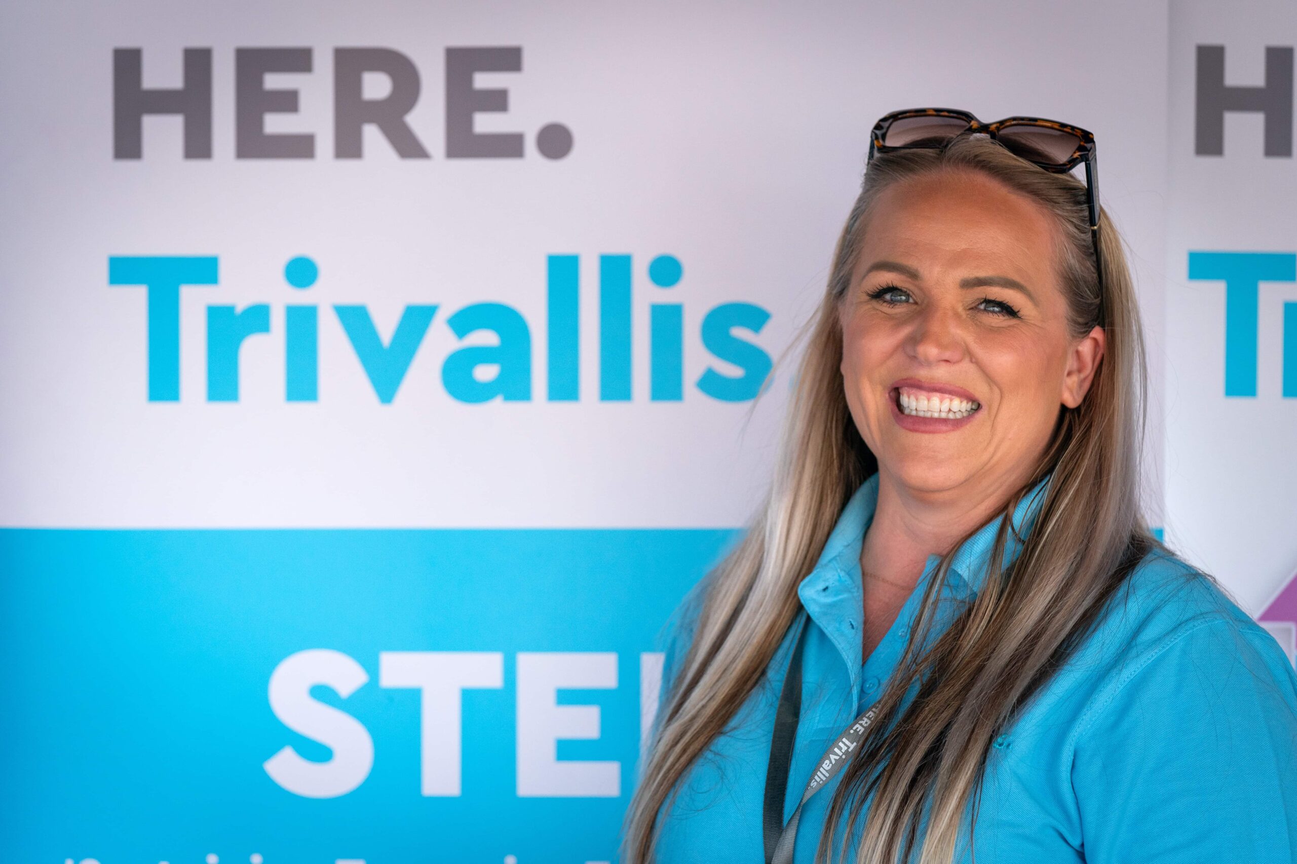 Trivallis Housing Landlord Wales Smiling professional woman in a blue polo shirt standing before a Trivallis Community Housing promotional backdrop.