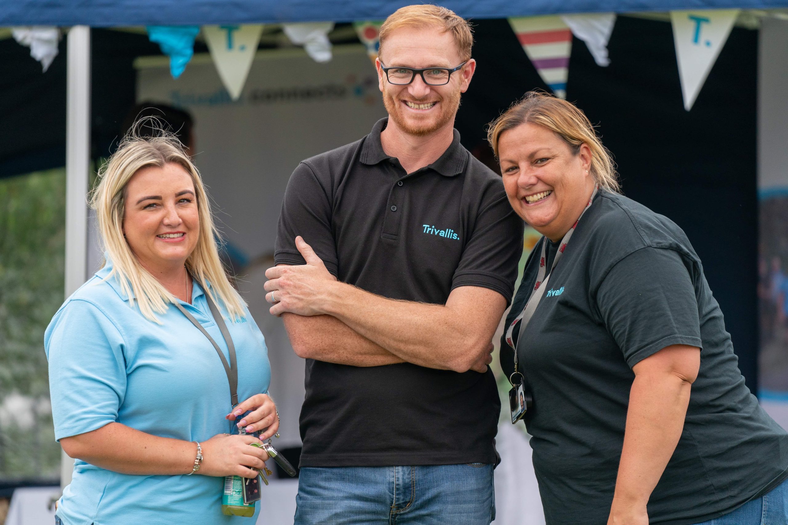 Trivallis Housing Landlord Wales Three smiling colleagues from Trivallis Community Housing posing at an outdoor event, with one woman holding a set of keys and another giving a thumbs-up, suggesting a positive and successful team experience.