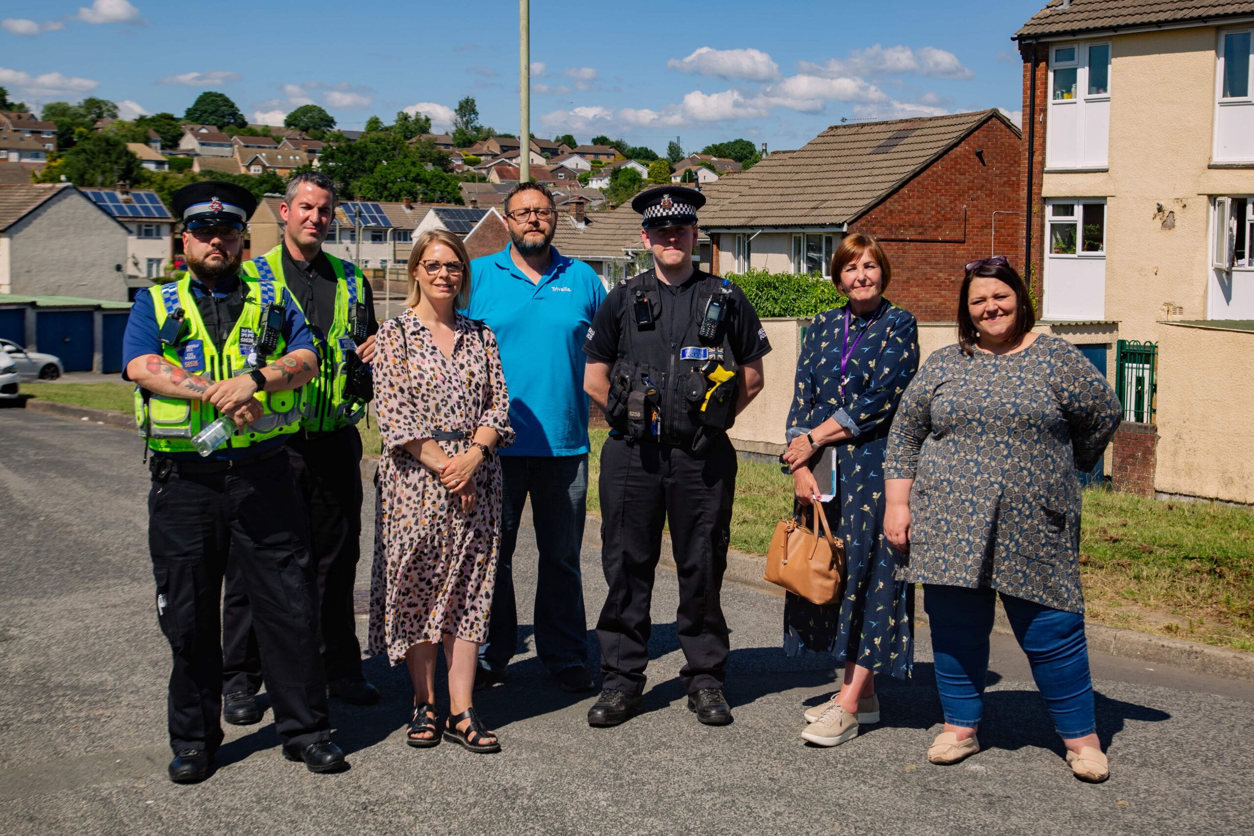 Trivallis Housing Landlord Wales A group of Trivallis Community Housing members standing together on a residential street on a sunny day, including police officers and civilians likely collaborating on a local safety or neighborhood initiative.