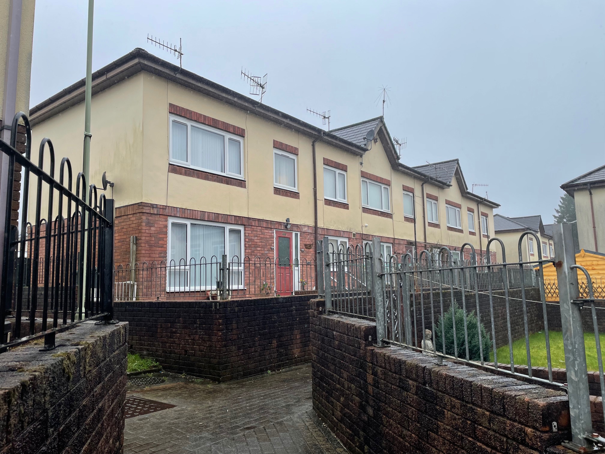 A row of modern terraced houses on an overcast day, featuring brick fences and metal gates.