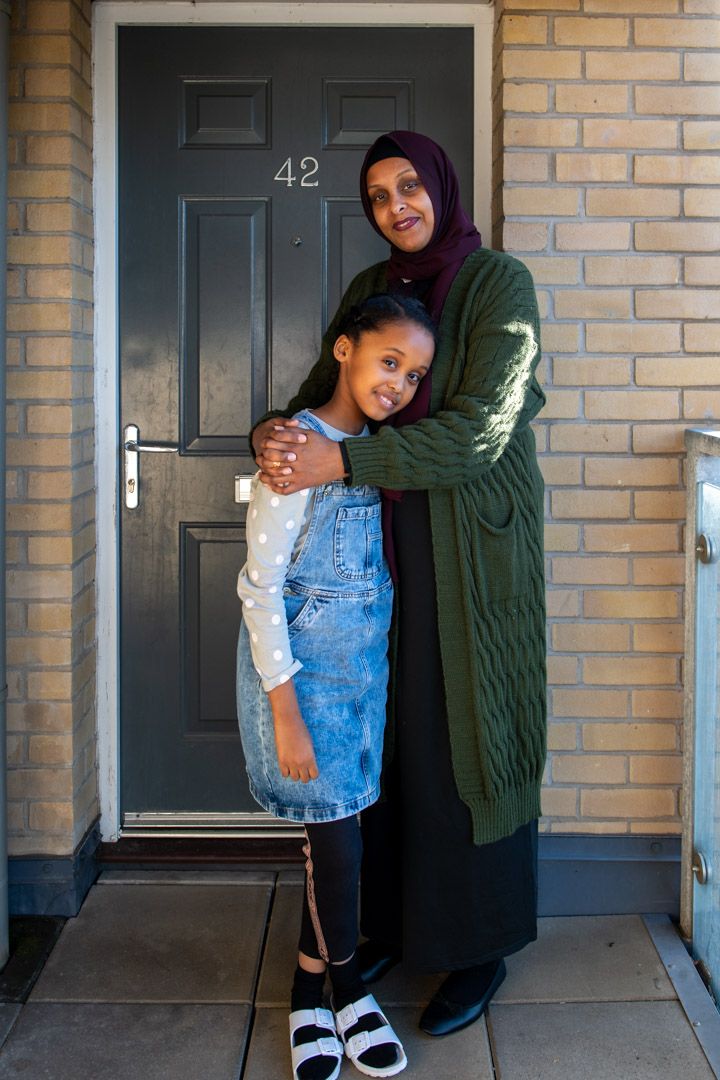 Trivallis Housing Landlord Wales A woman and a young girl stand together in a warm embrace outside a Trivallis housing with the number 42 on the door; the woman is wearing a hijab and a long cardigan,