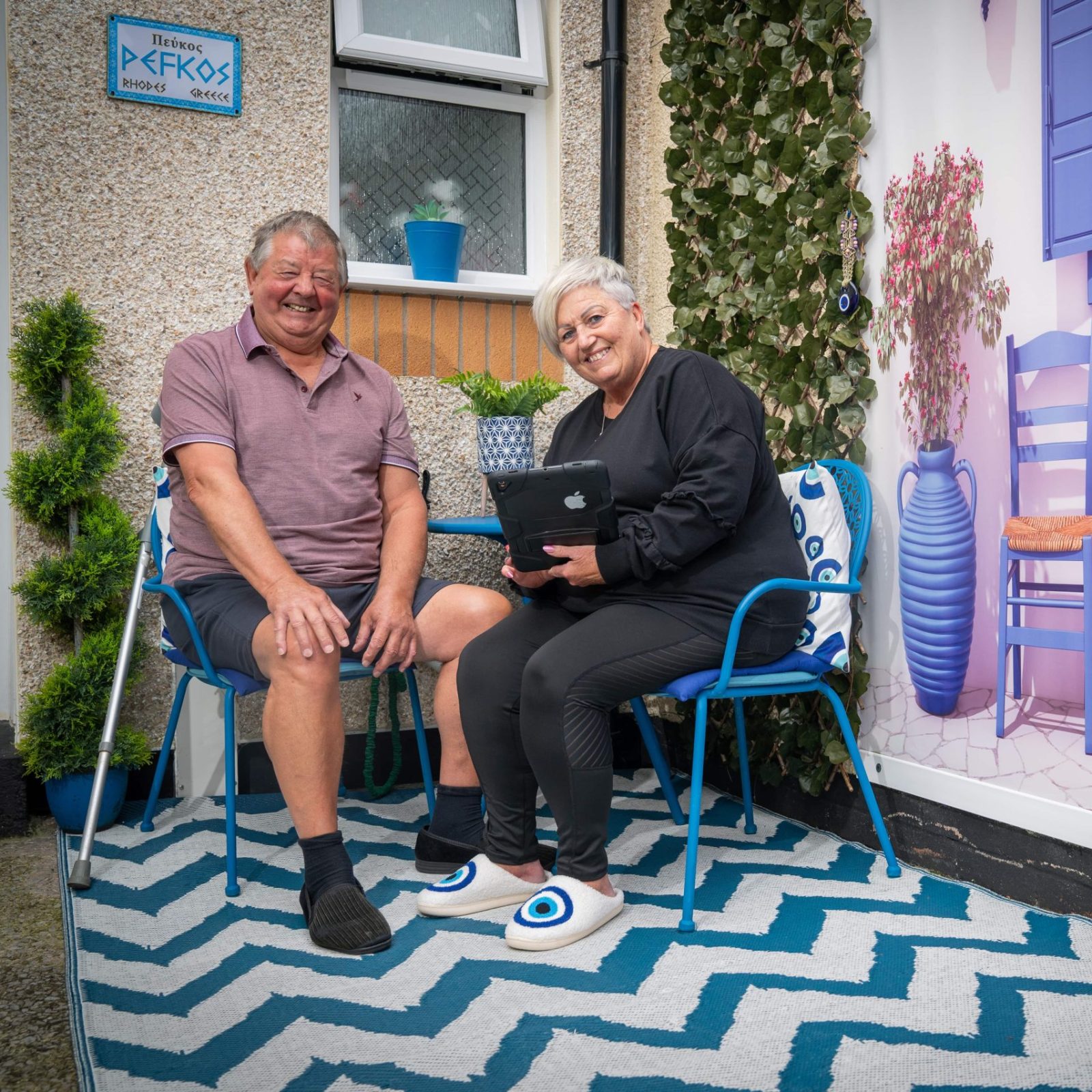 Trivallis Housing Landlord Wales A man and a woman sit outside a house with a decorative facade featuring a painted scene of a cafe, complete with a statue and a patterned rug, part of Trivallis' RCT housing