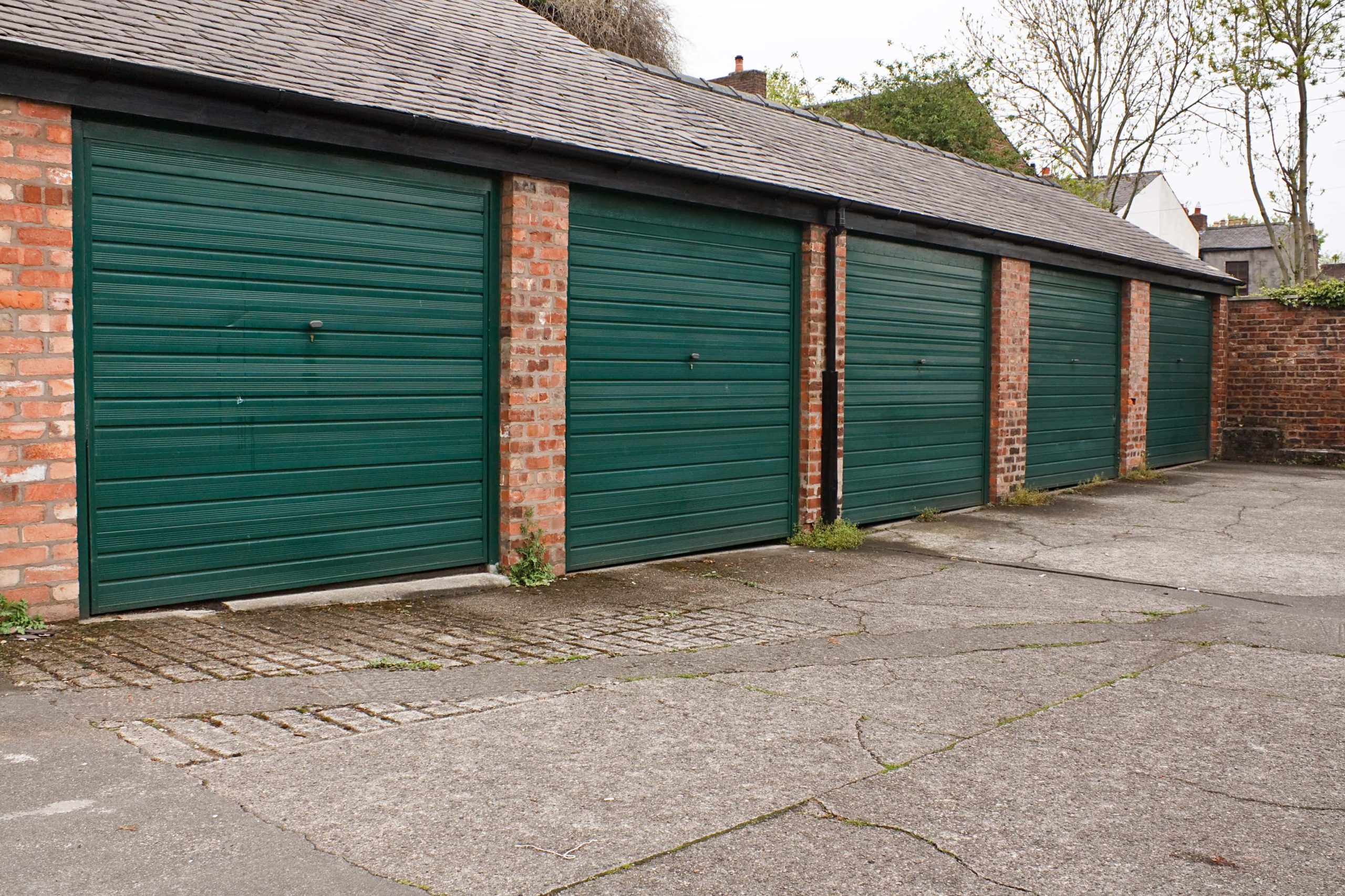 Trivallis Housing Landlord Wales A row of green garage doors along a Trivallis housing brick building, with a paved area in the foreground.