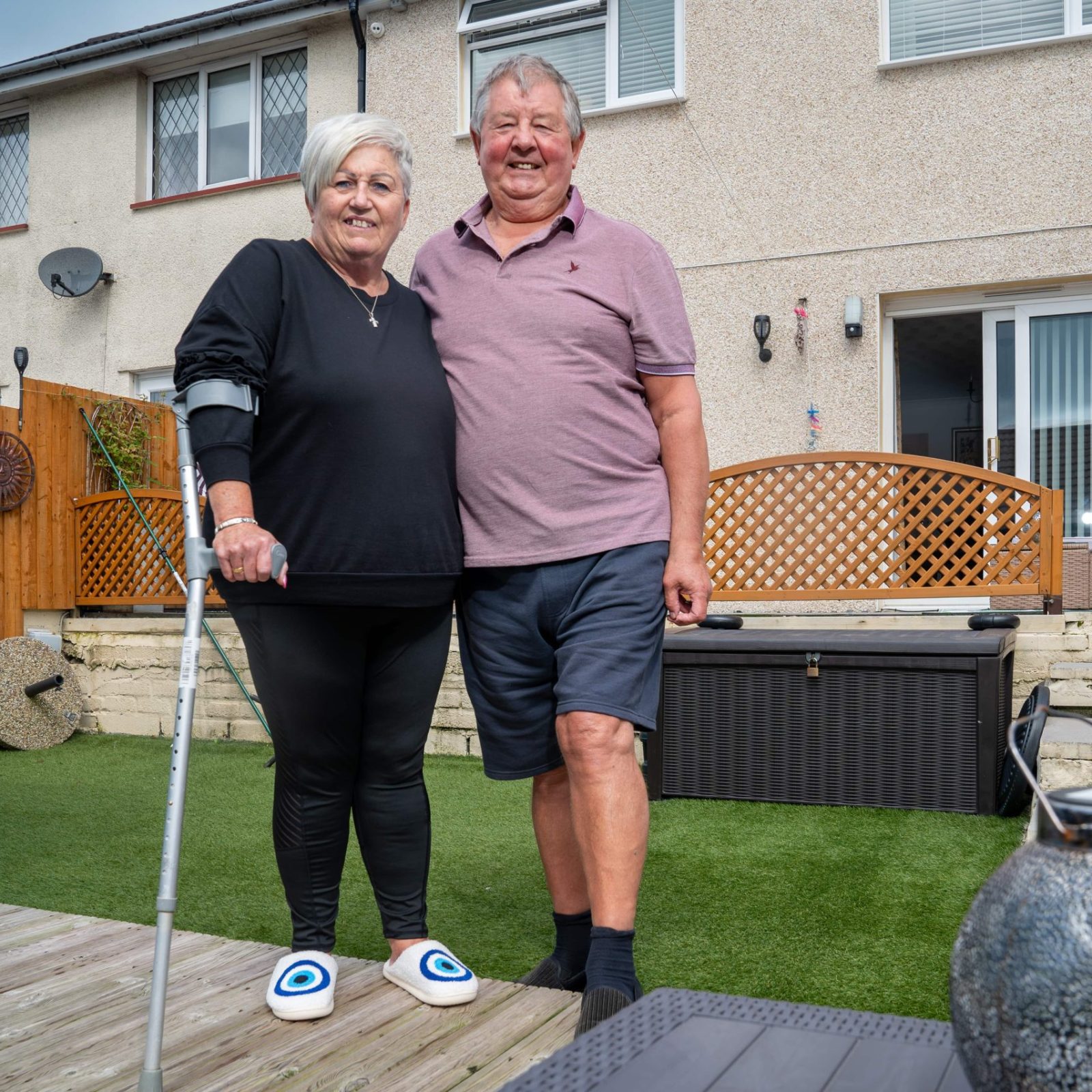Trivallis Housing Landlord Wales A smiling couple stands together in the backyard of a Trivallis housing residential home, with the woman holding onto a cane and a man with his arm around her.