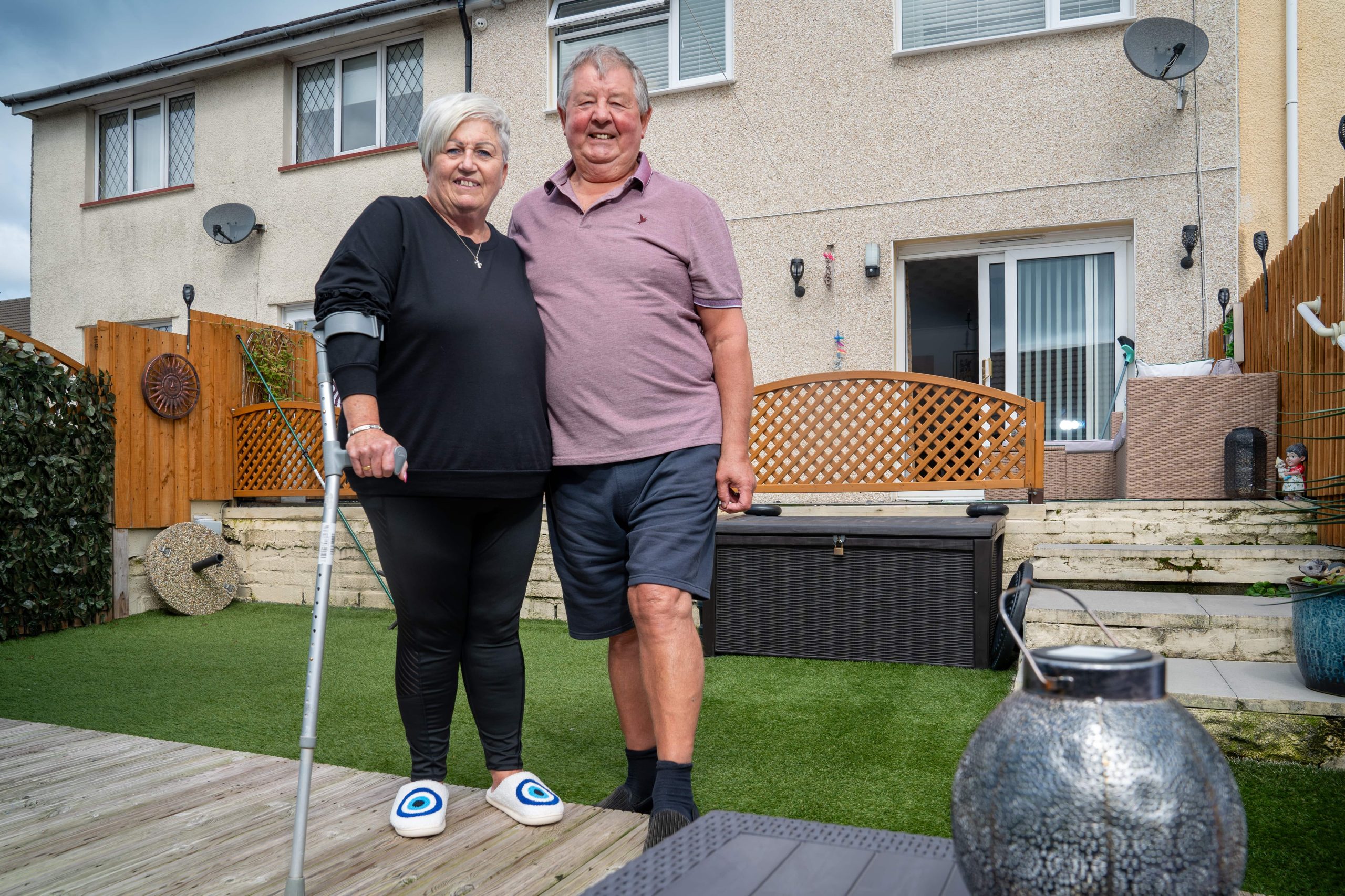 Trivallis Housing Landlord Wales A smiling couple stands together in the backyard of a Trivallis housing residential home, with the woman holding onto a cane and a man with his arm around her.