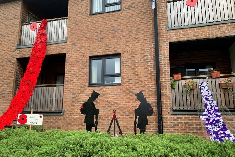 Trivallis Housing Landlord Wales A Trivallis housing building facade with two large red poppy flower decorations, silhouette figures of soldiers, and smaller poppy adornments commemorating Remembrance Day in RCT.