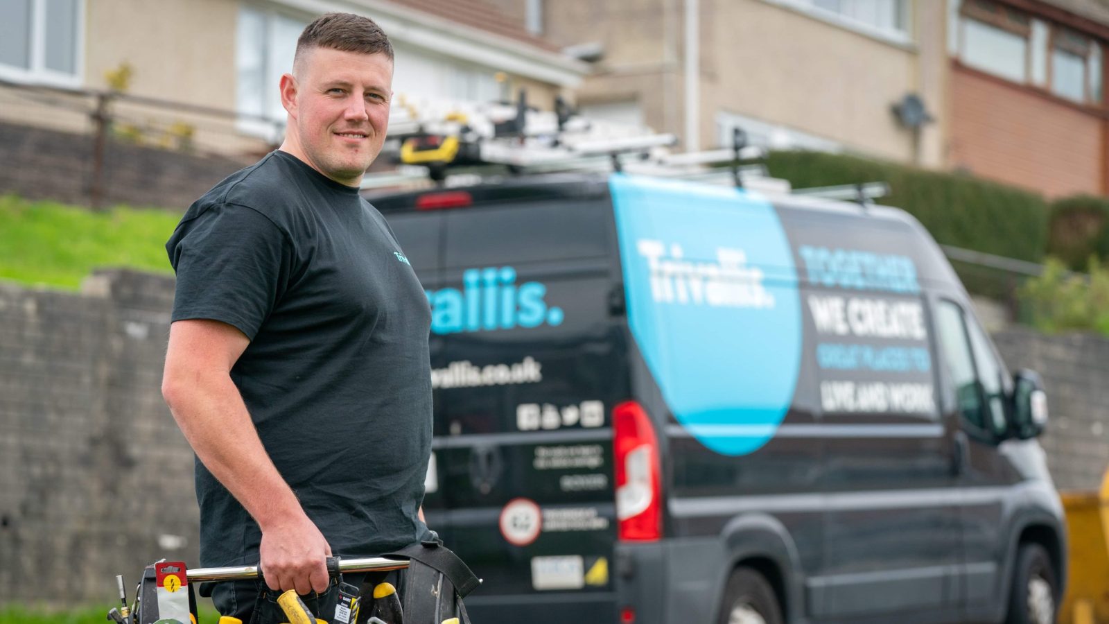 A man carrying a toolbox smiling in front of a service van with 