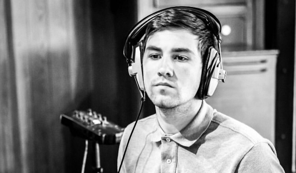 A young man in a studio wearing headphones plays an electronic drum pad, looking intently at the instrument. the photo is in black and white, highlighting his focused expression.