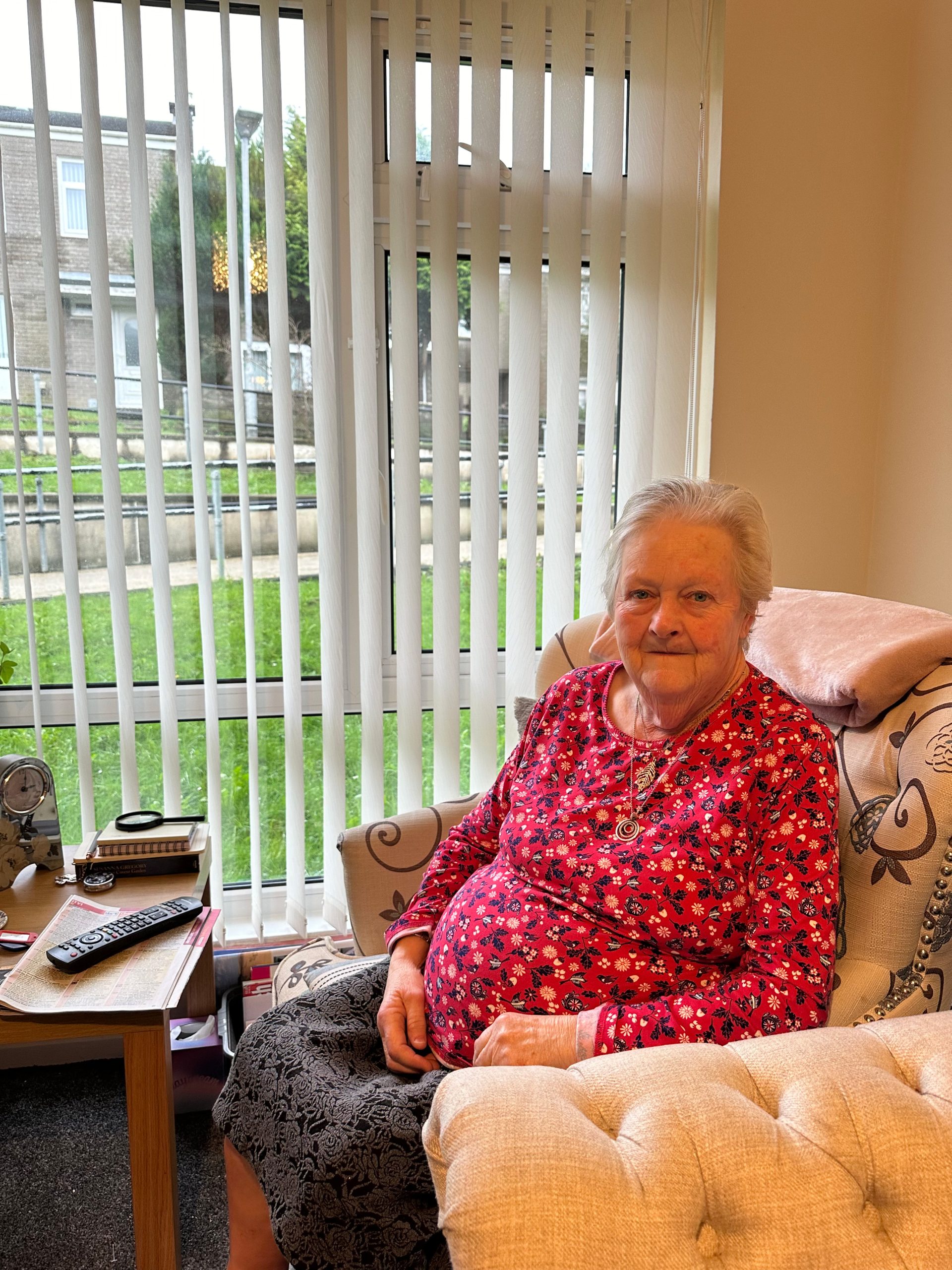 Trivallis Housing Landlord Wales An elderly lady sitting comfortably in a well-lit room with a pleasant smile, surrounded by a cozy home environment.