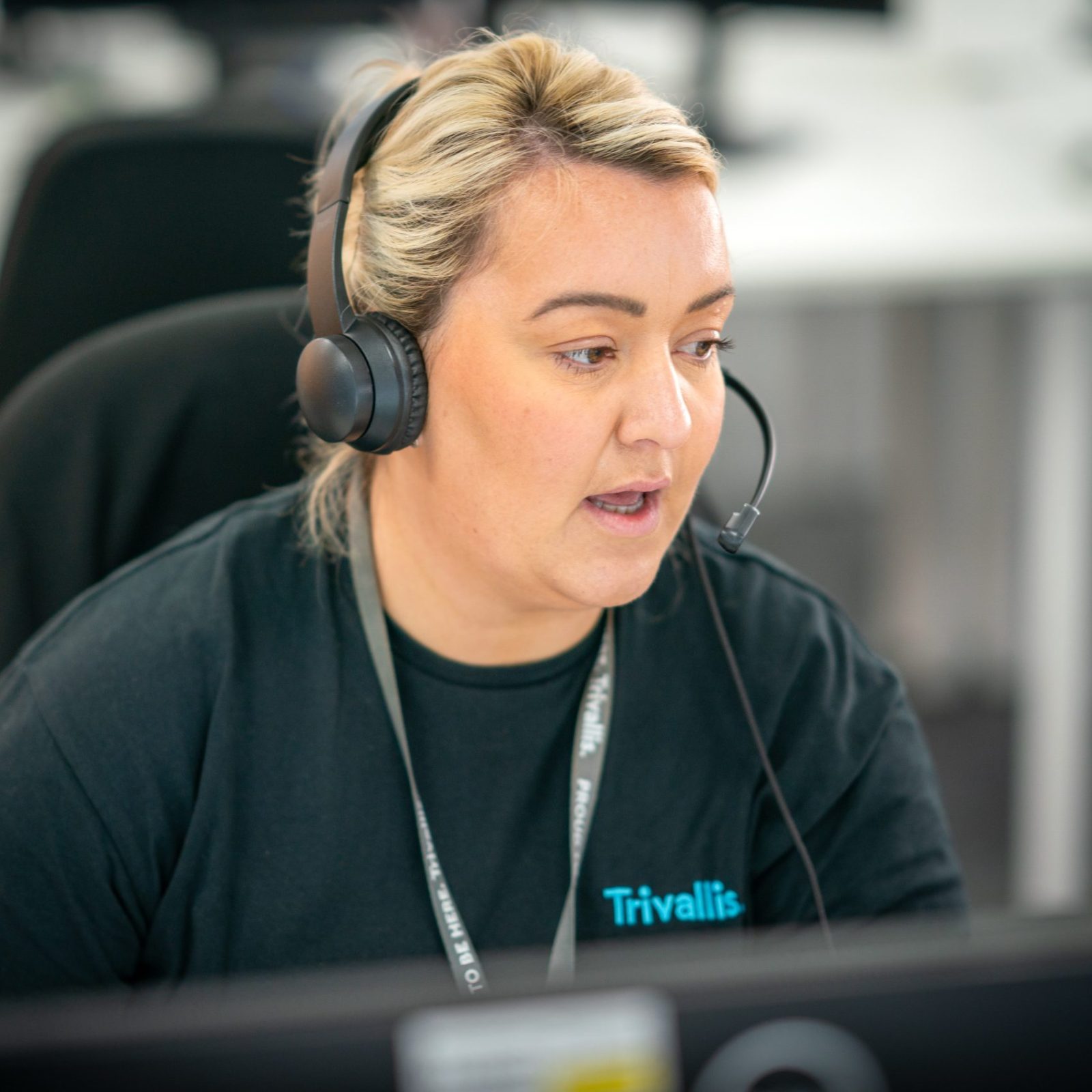 Trivallis Housing Landlord Wales A woman with short blonde hair, wearing a black t-shirt and headset, working at a computer in an office setting. she appears focused on her task. the name 
