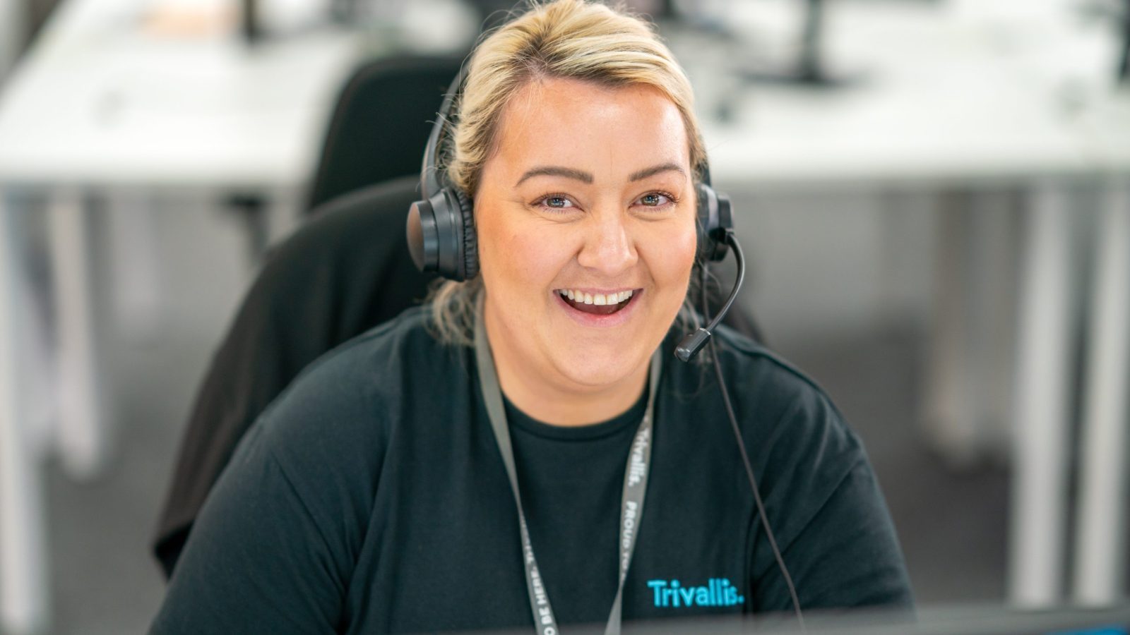 Trivallis Housing Landlord Wales A cheerful woman with blonde hair wearing a headset and a black shirt labelled 