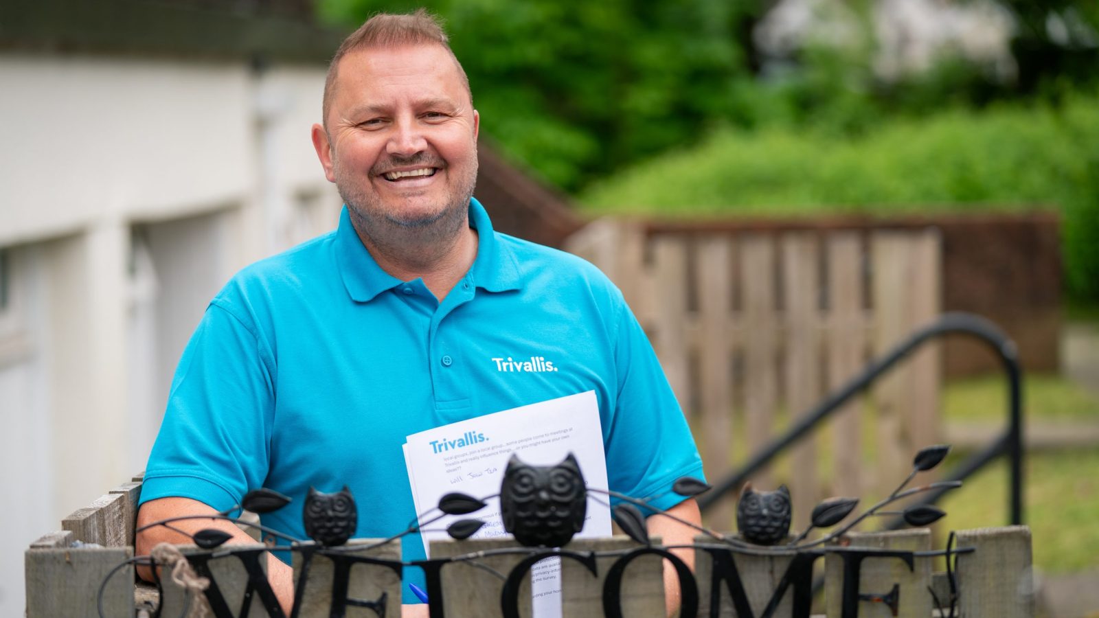 Trivallis Housing Landlord Wales A person in a blue shirt, holding a document, stands behind a decorative 