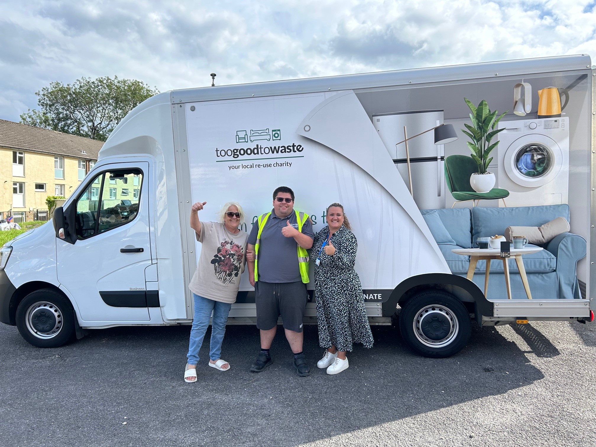 Trivallis Housing Landlord Wales Three people stand in front of a white delivery truck with a logo and text reading "toogoodtowaste your local re-use charity." The truck features images of household items on the side. The individuals appear to be acknowledging the camera with gestures.