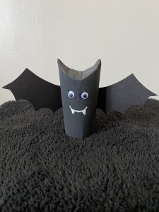 Trivallis Housing Landlord Wales A black cardboard tube is decorated as a bat with googly eyes, paper fangs, and paper wings. It stands on a textured black surface against a plain background.