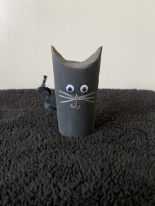 Trivallis Housing Landlord Wales A small cat figurine made from a painted cardboard tube stands on a dark textured surface. It features googly eyes, drawn-on whiskers, and a curled pipe cleaner for a tail.