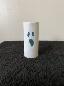 Trivallis Housing Landlord Wales A cardboard toilet paper roll stands upright on a dark textured surface. It is painted white with a simple ghost face drawn in black, featuring two oval eyes and an open mouth, set against a plain light-colored background.