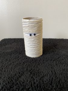 Trivallis Housing Landlord Wales A cardboard tube wrapped in white string stands upright on a textured black surface. Two small googly eyes are attached to the string, giving the tube a playful appearance.