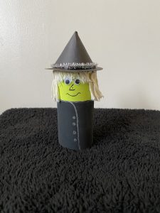 Trivallis Housing Landlord Wales A handmade witch figure stands on a black textured surface. It is made from a painted cylindrical base with a green face, blonde yarn hair, and a conical black hat decorated with silver trim.