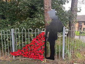 Trivallis Housing Landlord Wales A silhouette of a soldier is mounted on a fence beside a tree. Red poppies are arranged at the base, cascading onto the ground. Houses are visible in the background.