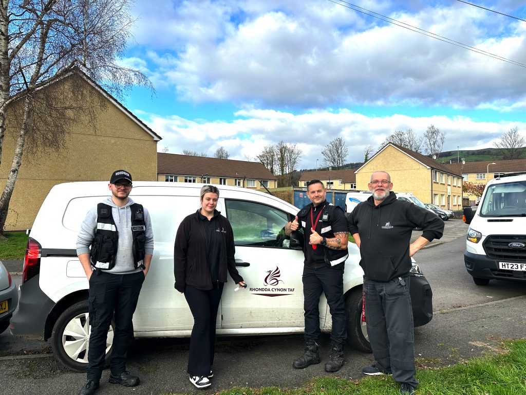 Trivallis Housing Landlord Wales Four people are standing in front of a white van with "SUNDORNA CYNON TAF" written on it. They are outdoors near residential buildings, and the sky is partly cloudy.