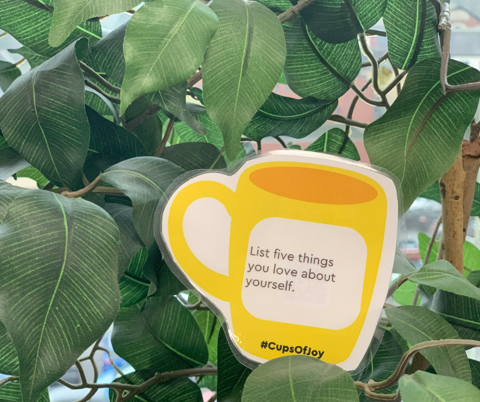 Trivallis Housing Landlord Wales A yellow paper cup cutout with the text "List five things you love about yourself" is attached to a leafy green plant. The hashtag "#CupsOfJoy" appears at the bottom.