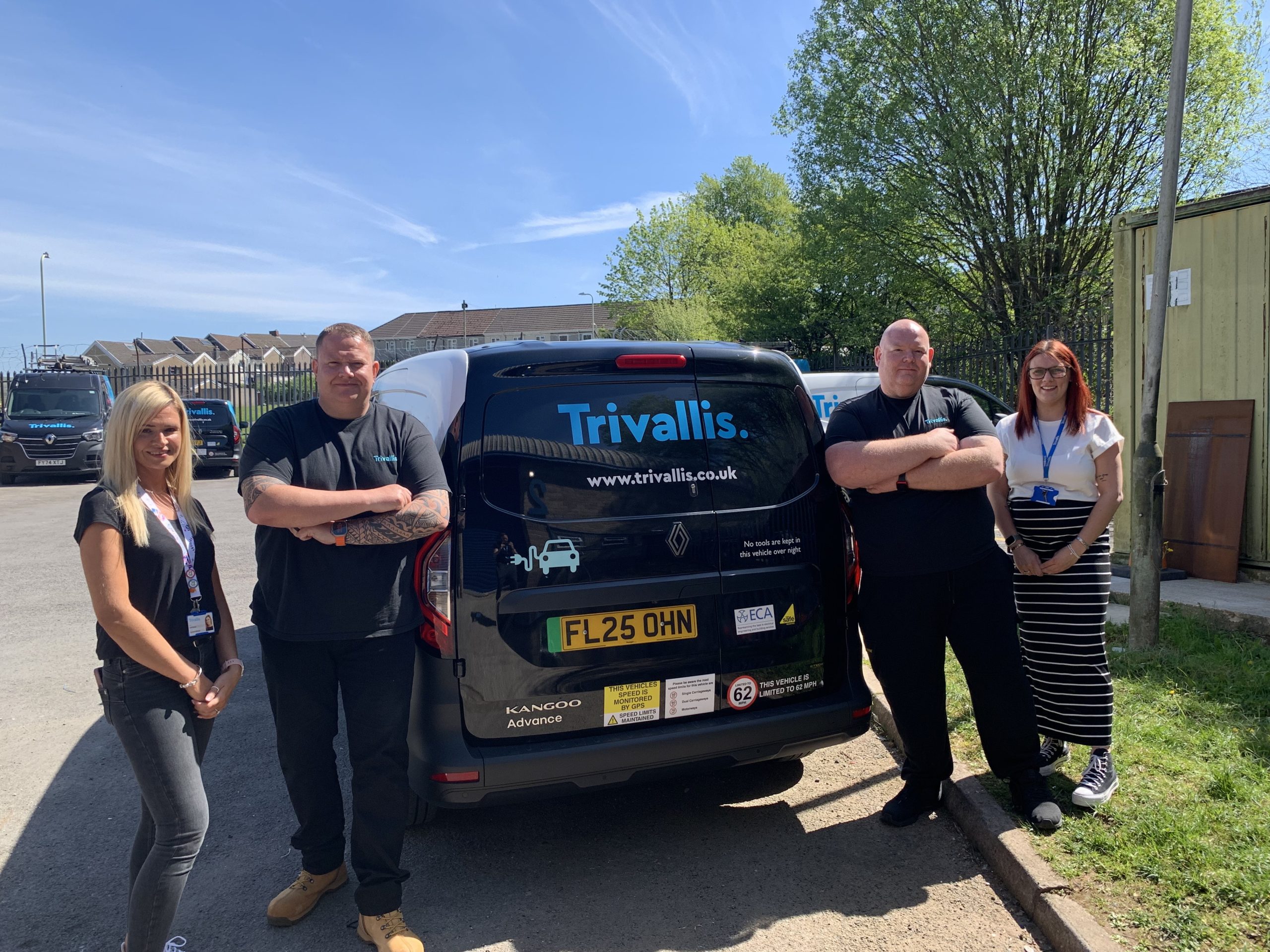 Trivallis Housing Landlord Wales Four people stand next to a black van with “Trivallis” branding on the back. The group is outdoors in a sunny area with trees, a fence, and a yellow building visible in the background.