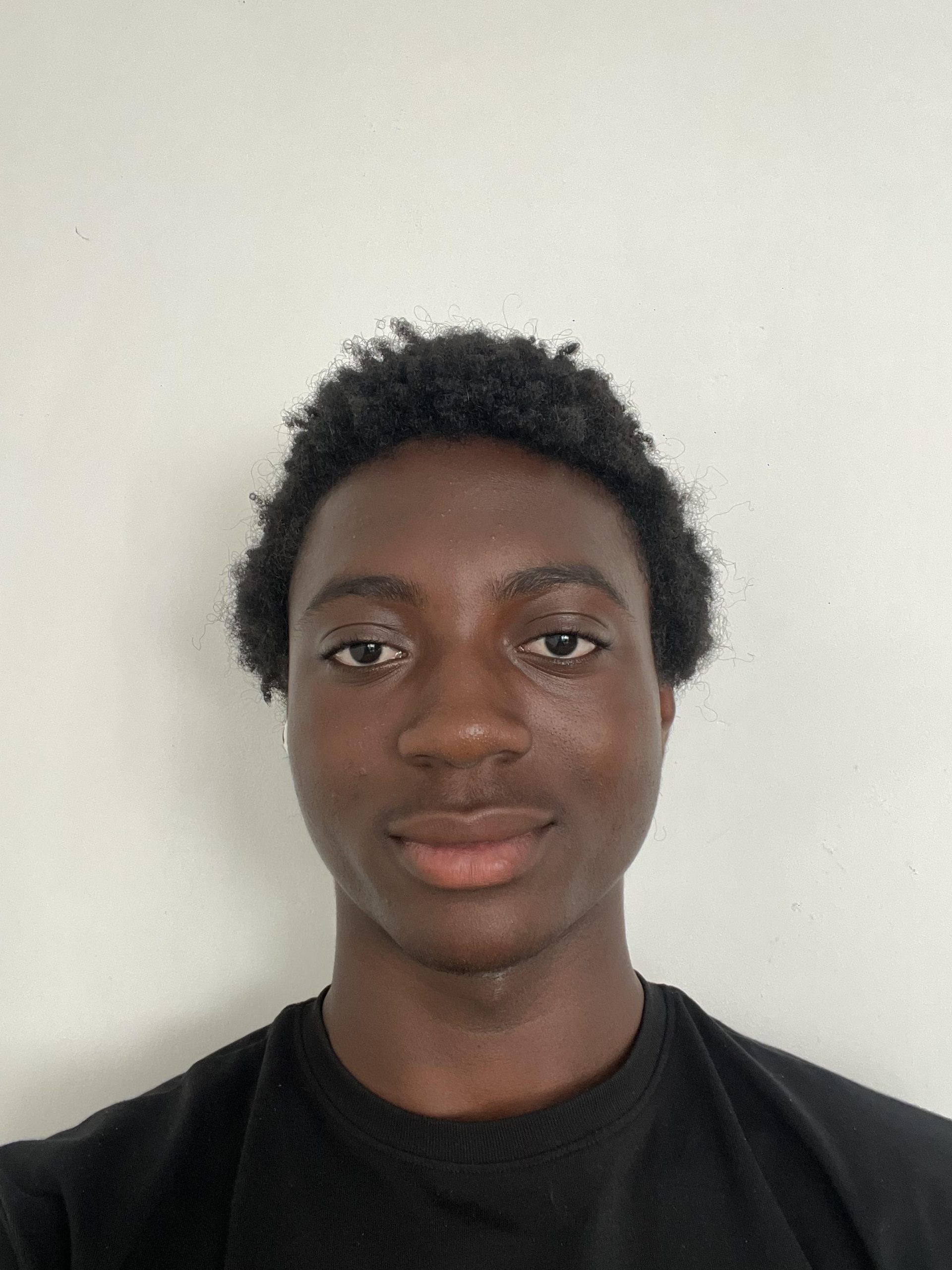 Trivallis Housing Landlord Wales A young person with short curly hair and medium-dark skin wears a black shirt and looks at the camera with a neutral expression against a plain white background.