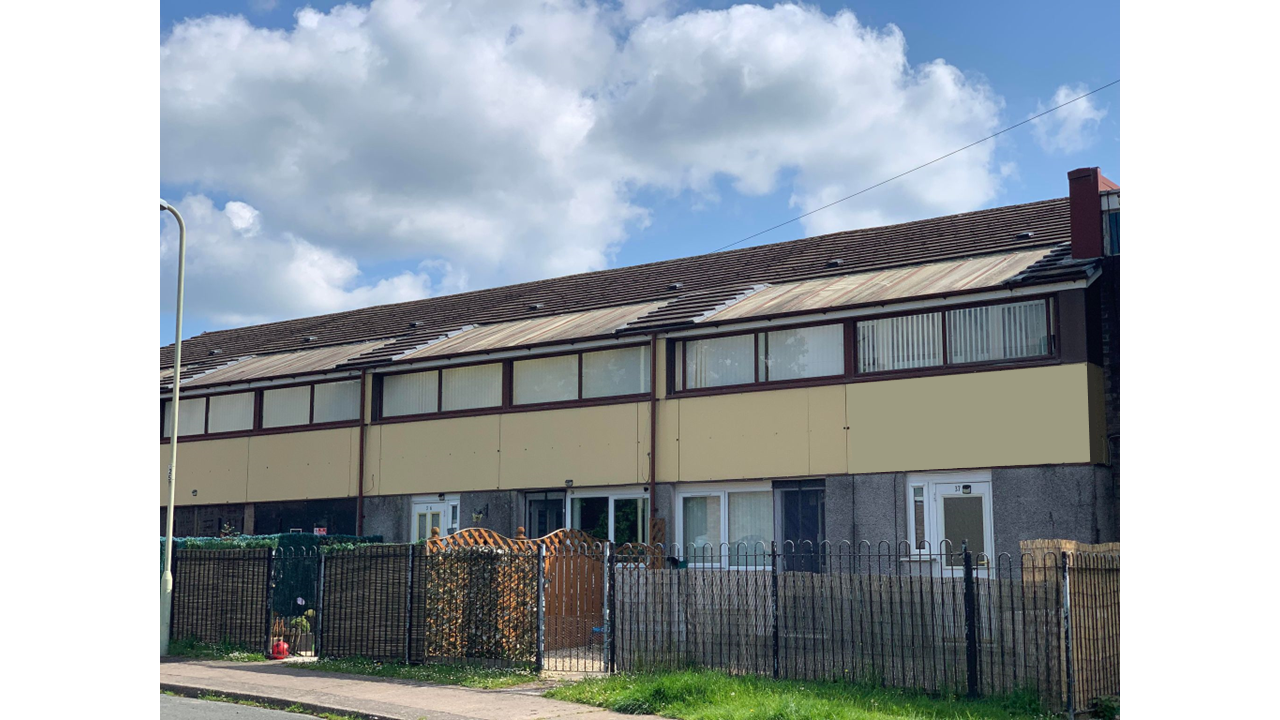 Trivallis Housing Landlord Wales A row of two-storey terraced houses with beige panels and brown trim, fenced front gardens, and patchy grass under a partly cloudy sky. Curtains and blinds cover most windows.